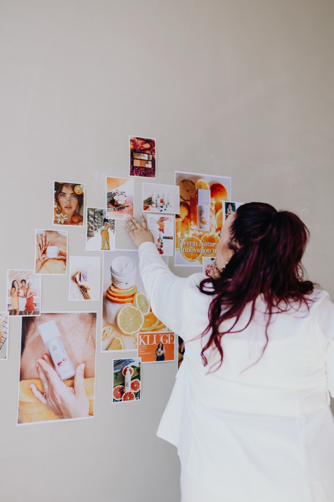 Nadine Kluge in Weiß, von hinten, hängt Bilder an ihre Moodboard-Wand